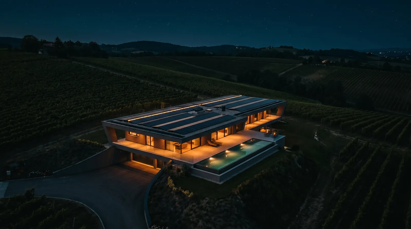 Villa moderna vista dall'alto di notte, pannelli sul tetto e piscina illuminata tra i vigneti